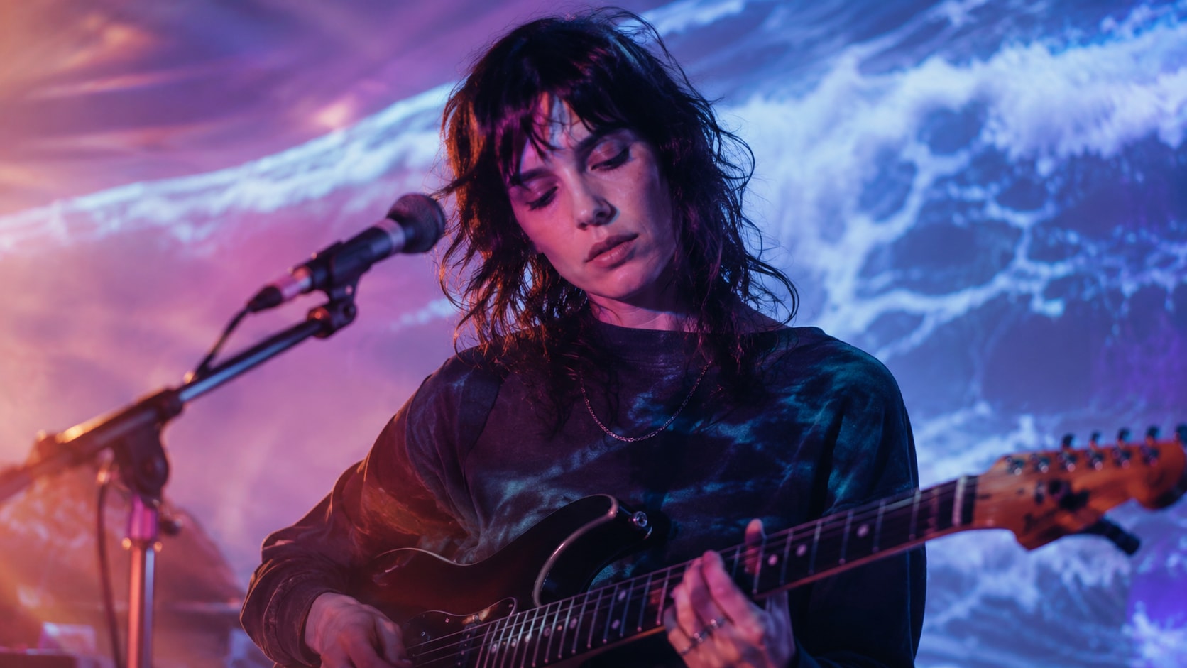 Ada Lea performing live with her electric guitar on stage under atmospheric lighting.
