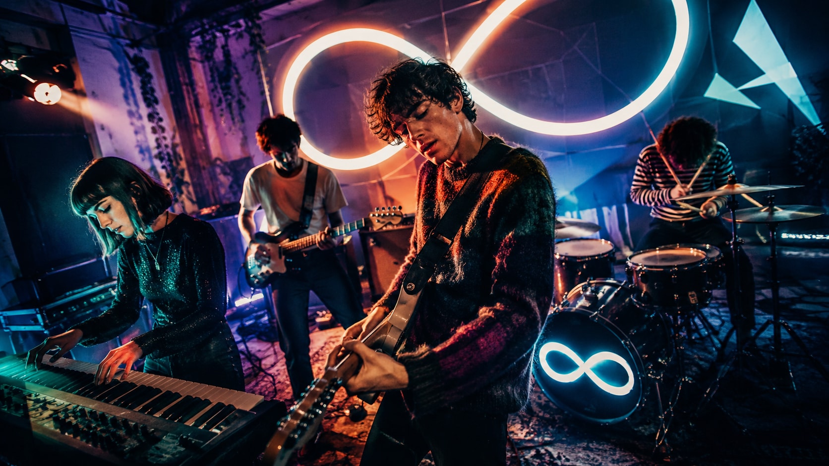 Myth Math performing live under bright neon infinity symbols.