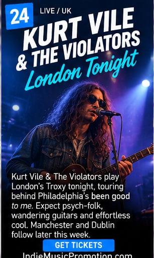 Kurt Vile singing into vintage microphone under blue and purple stage lights.