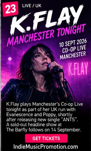 K.Flay singing into microphone with eyes closed under purple spotlights.