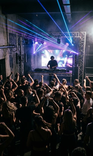 Underground Belfast dance club with DJ behind decks and vibrant laser lights for DAIRE The Connection Tour.